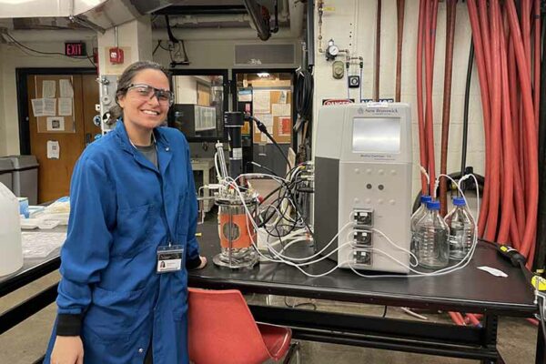 student smiling in lab coat in lab with bioreactor equipment