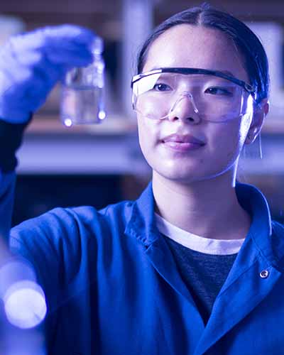 female asian student in lab coat holding up lab glass in chemistry lab